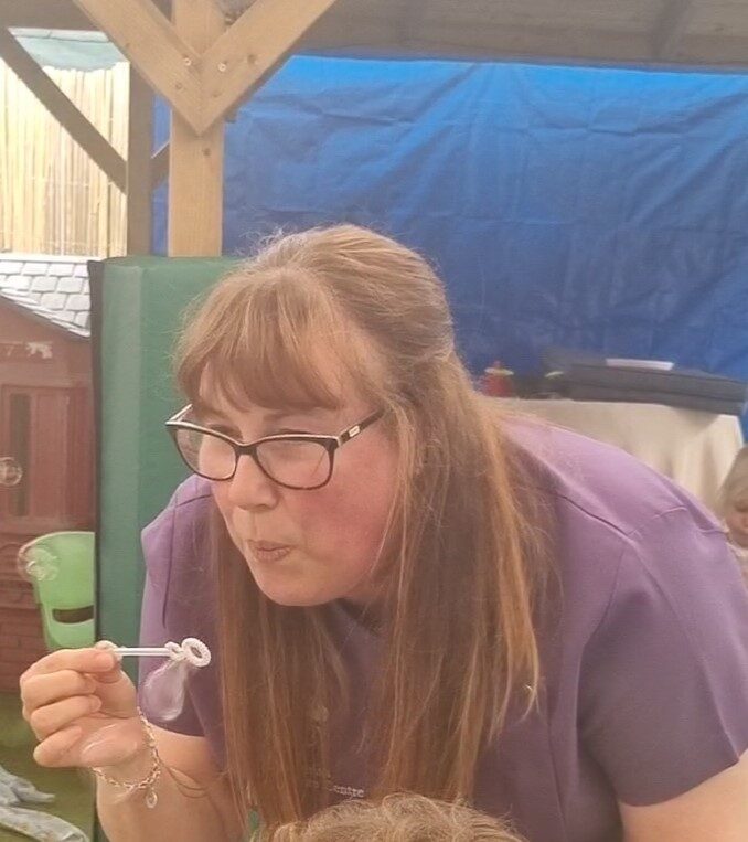 Linda, a member of staff, blowing bubbles with children outdoors
